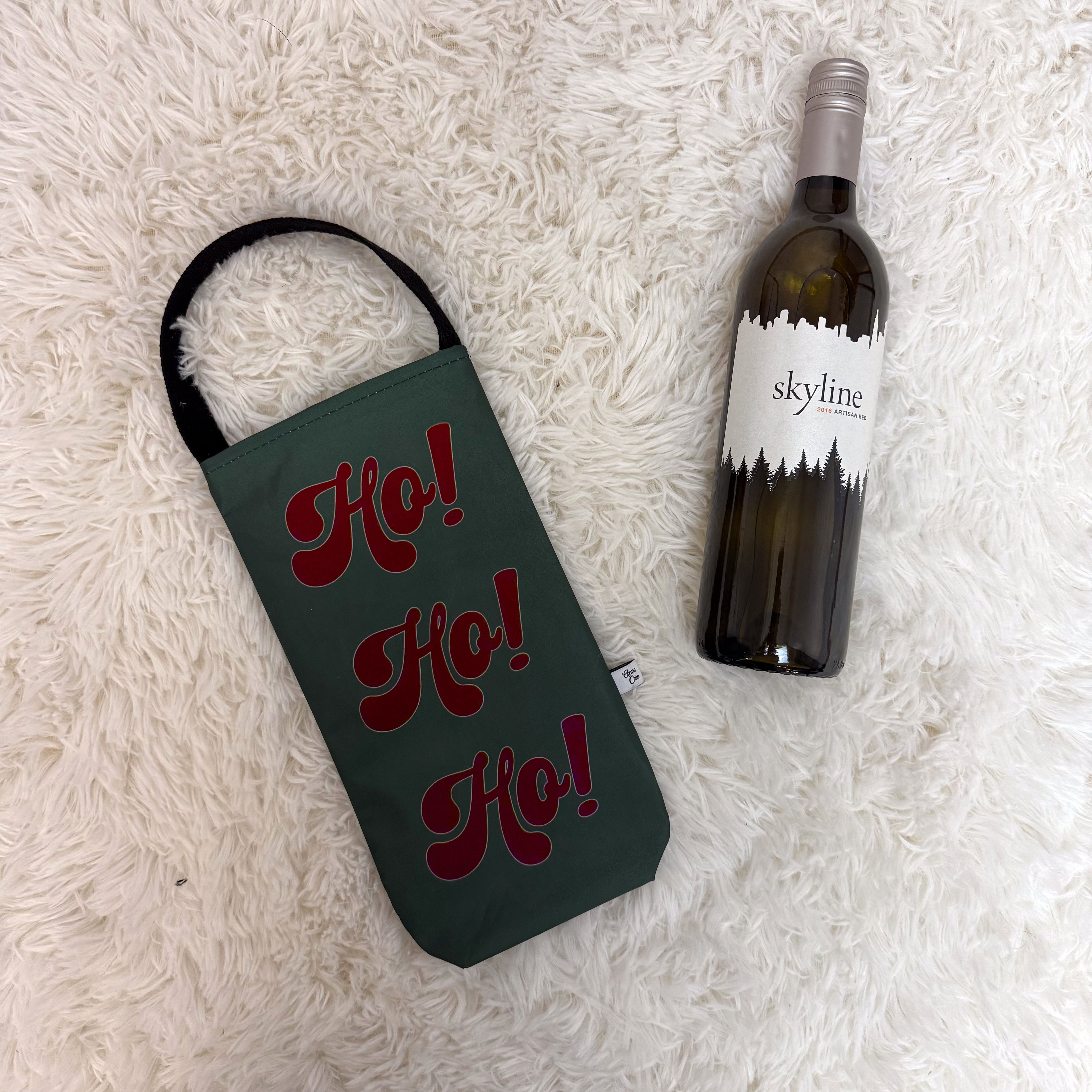 Wine bottle with 'Ho! Ho! Ho!' holder and 'skyline' wine bottle on a textured white surface