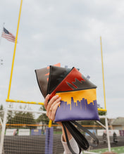 Person holding a colorful bag with a cityscape design on a sports field background